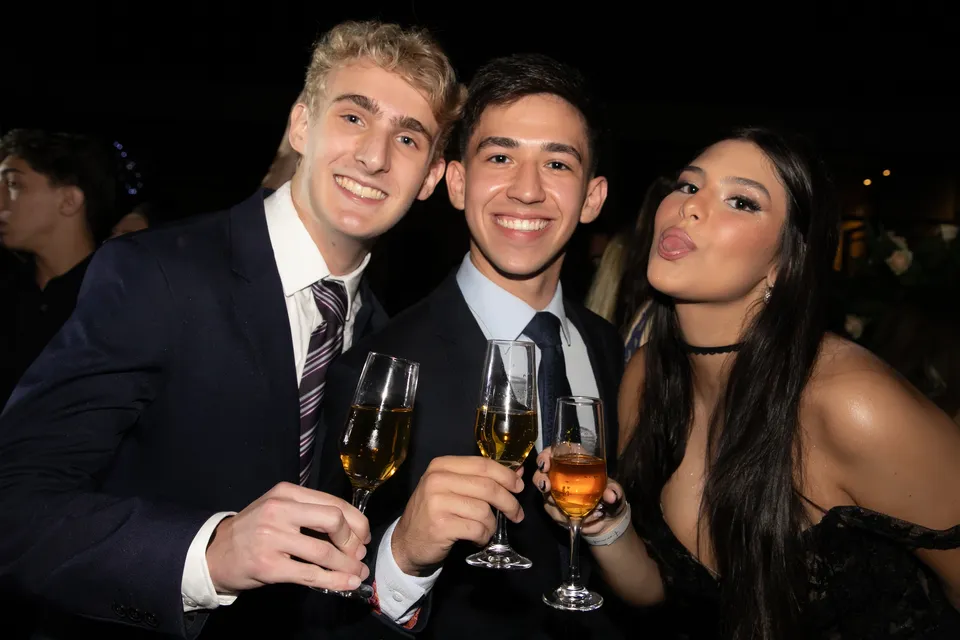 Três convidados sorrindo e brindando com taças no baile